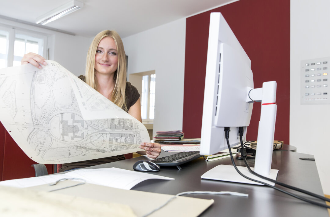 Eine Katastertechnikerin sitzt am Schreibtisch und hält eine Flurkarte in den Händen